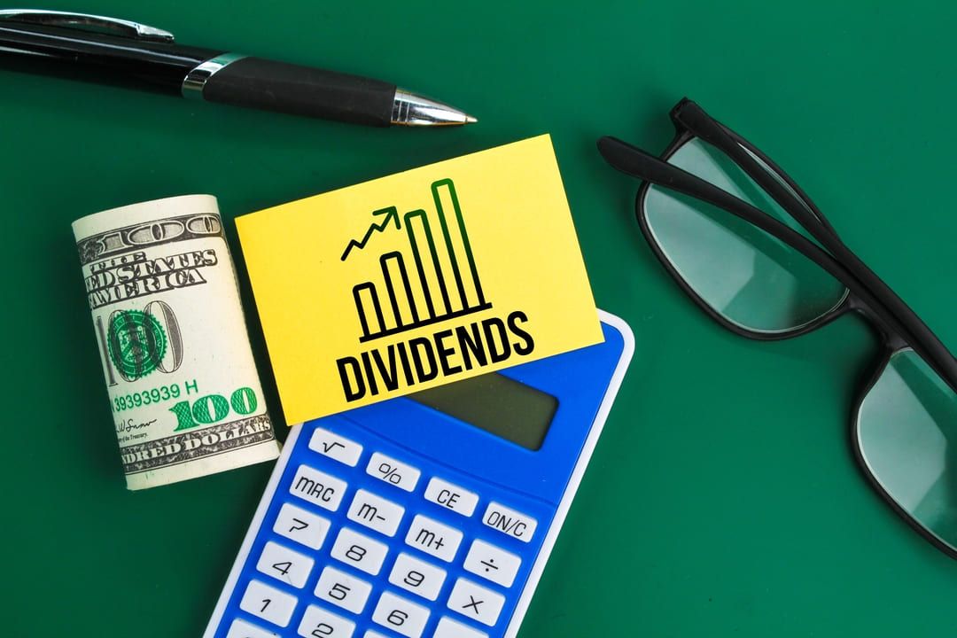 Óculos, notas de dólares, calculadora, caneta e papel escrito dividendos sob superfície verde