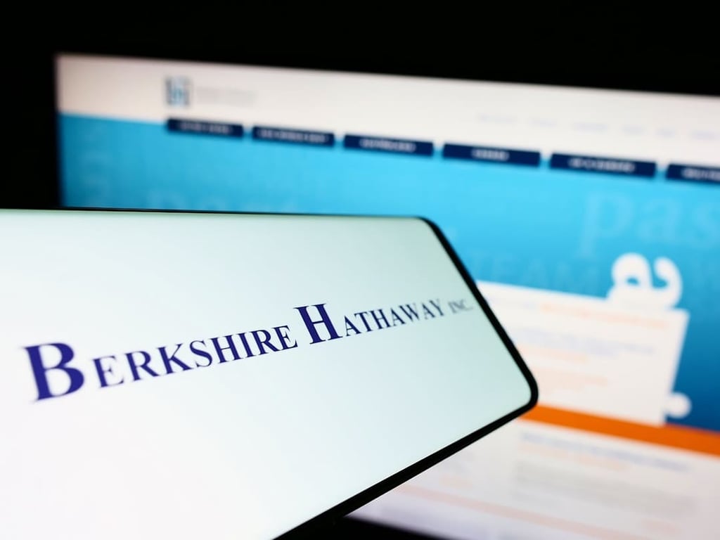 Celular com logo da Berkshire Hathaway com tela de computador ao fundo desfocada
